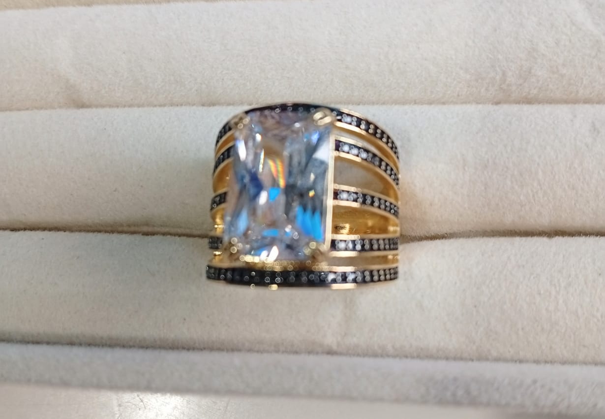 Anel Powerstone, folheado a ouro 18K, com pedra quadrada de zircônia e cravejado com micro zircônias negras.